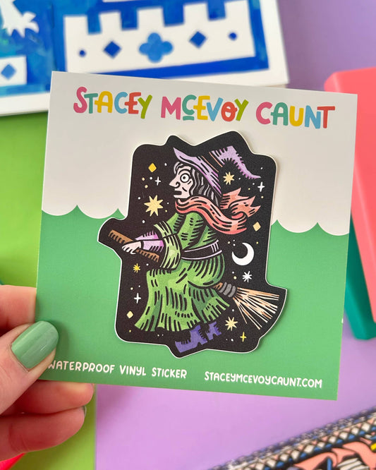 The witch on a broomstick vinyl sticker is shown on a green and white backing card with colourful "Stacey McEvoy Caunt" branding. The card highlights the sticker’s waterproof vinyl quality and website details. A colourful and fun product from Rebel Romance, a UK small business specialising in bold gifts and alternative style.