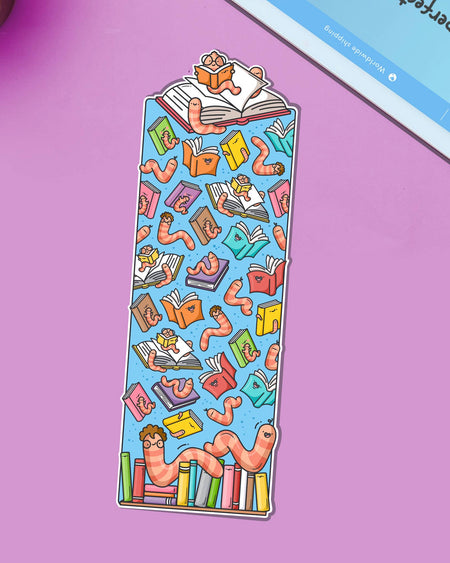 Colourful bookworm bookmark by Toastedink, sold by Rebel Romance, featuring cheerful cartoon worms with glasses surrounded by smiling books on a blue background. Displayed on a purple backdrop.