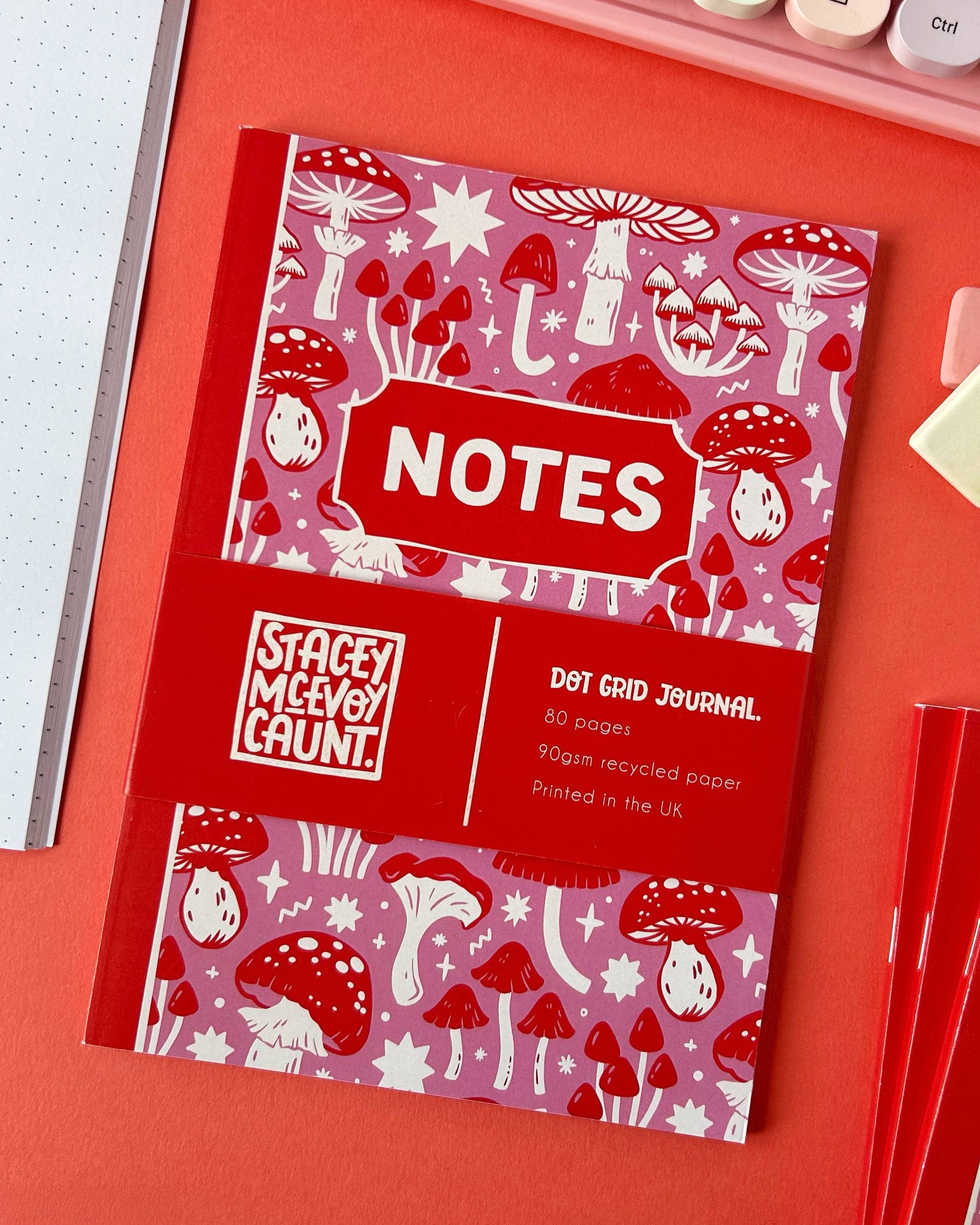 Overhead view of a Stacey McEvoy Caunt mushroom notebook by Rebel Romance. The colourful pink and red cover is decorated with magical mushroom illustrations, and the band states it's printed in the UK on recycled paper.