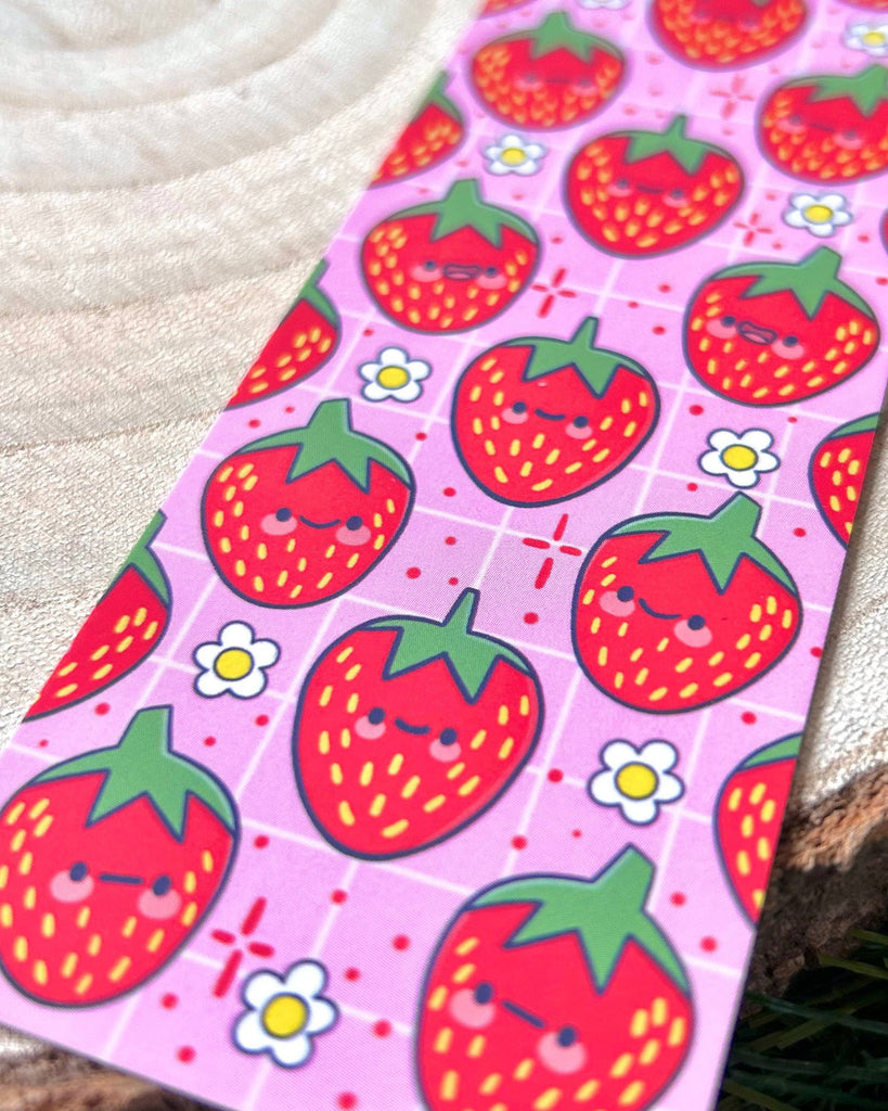 Close-up of the Berry Cute Strawberries Bookmark by Kelly Lou, available from Rebel Romance. The cheerful pink design shows rows of happy red strawberries with green leaves and scattered daisies, bringing fun, playful vibes to your reading routine.