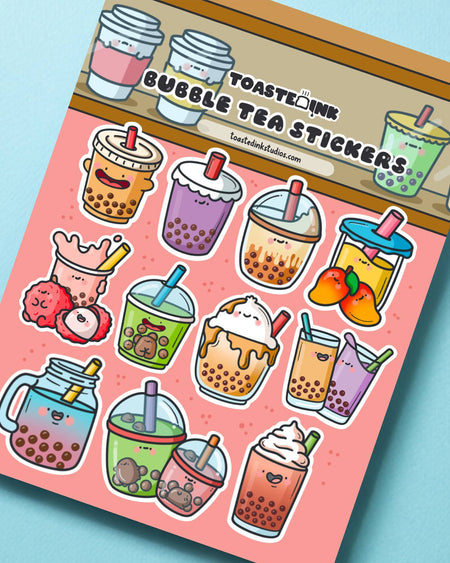 Angled shot of Toastedink’s Bubble Tea Sticker Sheet on a bright blue surface. Includes smiling bubble tea designs with tapioca pearls and fruity toppings. Stocked by Rebel Romance, ideal for laptops, journals and gift wrapping.