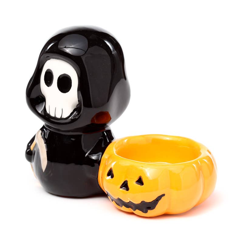 Front angled view of the ceramic tea light candle holder featuring a glossy black Skull Boy figure next to an orange pumpkin bowl. A spooky yet cute home accessory from Rebel Romance, perfect for Halloween or gothic-inspired décor lovers.