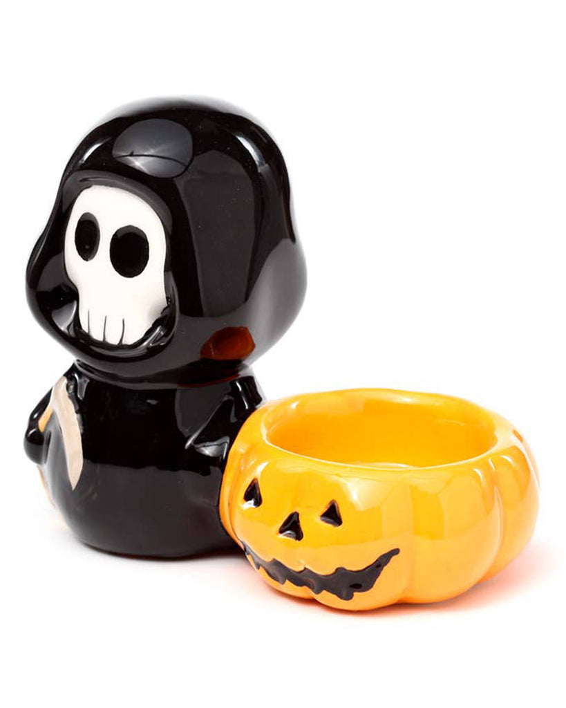 Front angled view of the ceramic tea light candle holder featuring a glossy black Skull Boy figure next to an orange pumpkin bowl. A spooky yet cute home accessory from Rebel Romance, perfect for Halloween or gothic-inspired décor lovers.
