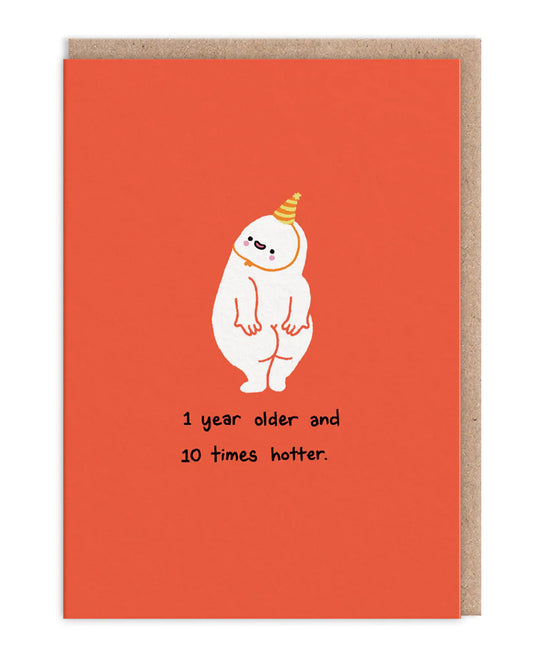 A6 funny birthday card from Rebel Romance featuring a cheeky white character in a party hat, standing proudly with a bashful expression on a bright red background. Text reads “1 year older and 10 times hotter.” Blank inside, with a brown kraft envelope. Designed by makingshit and stocked by Rebel Romance, a UK brand celebrating quirky and alternative aesthetics.