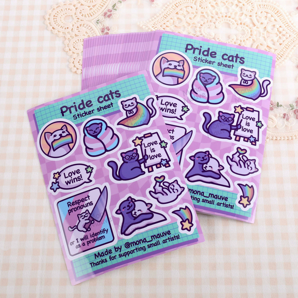 Two LGBTQ+ Pride Cats Sticker Sheets by Mona Mauve displayed on a soft, checkered surface. Each sheet includes 10 vinyl stickers with LGBTQ+ messages and cute cartoon cats, perfect for decorating journals, gifts, or laptops. Designed by a small artist to spread joy, inclusivity, and pride through art.