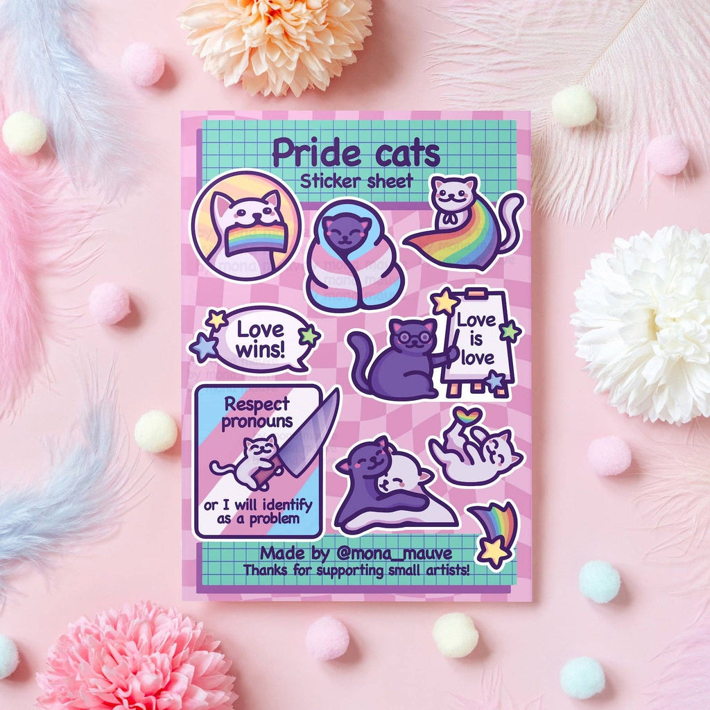 Flat lay of the LGBTQ+ Pride Cats Sticker Sheet by Mona Mauve, featuring 10 colourful vinyl stickers of cute illustrated cats holding pride flags, signs reading “Love is love” and “Respect pronouns,” and snuggling under rainbow blankets. Displayed on a pastel pink background with flowers and pompoms. A fun, queer-positive gift by a small artist.