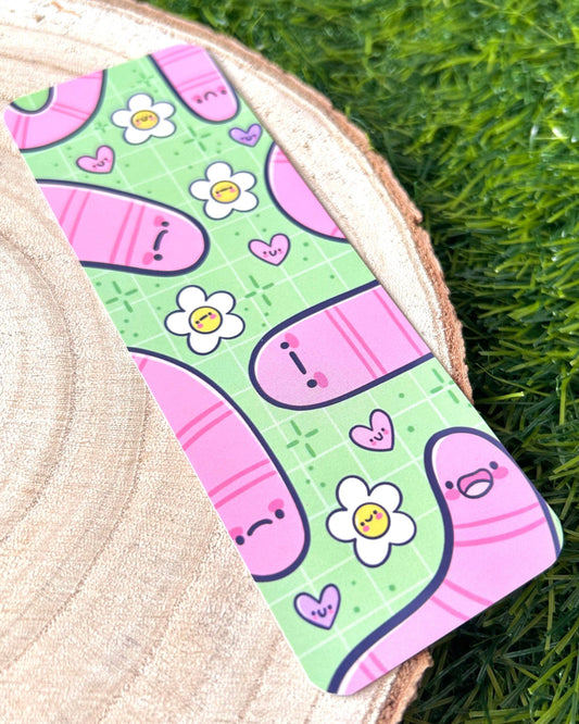 Flat lay of the Wormies Bookmark by Kelly Lou from Rebel Romance. The design shows cheerful pink worms, smiling daisies and cute hearts on a bright green patterned background. A fun, illustrated bookmark that reflects the small UK brand’s love for alternative, artistic aesthetics and unique gifts for millennials.