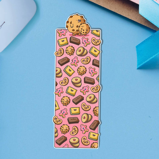 Glossy biscuit-themed bookmark featuring cartoon illustrations of cookies, pink iced biscuits, bourbons, jammy dodgers and other treats on a pink background. Topped with two cute chocolate chip cookies.
