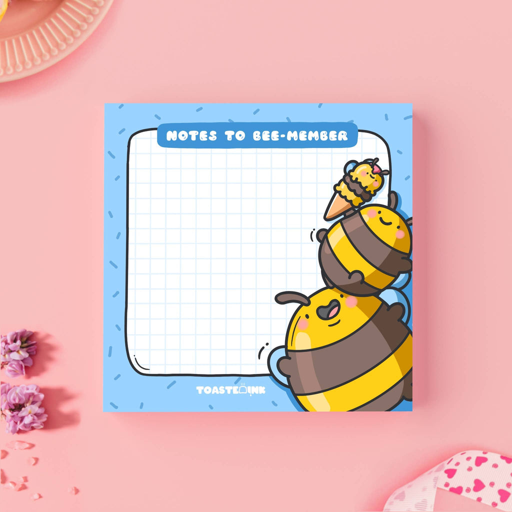 Square sticky note pad with a blue border and grid paper, featuring two chubby yellow and brown cartoon bumble bees stacking on top of each other to reach an ice cream. The top reads “Notes to Bee-member” in bold white text. Cute and practical stationery for daily reminders.