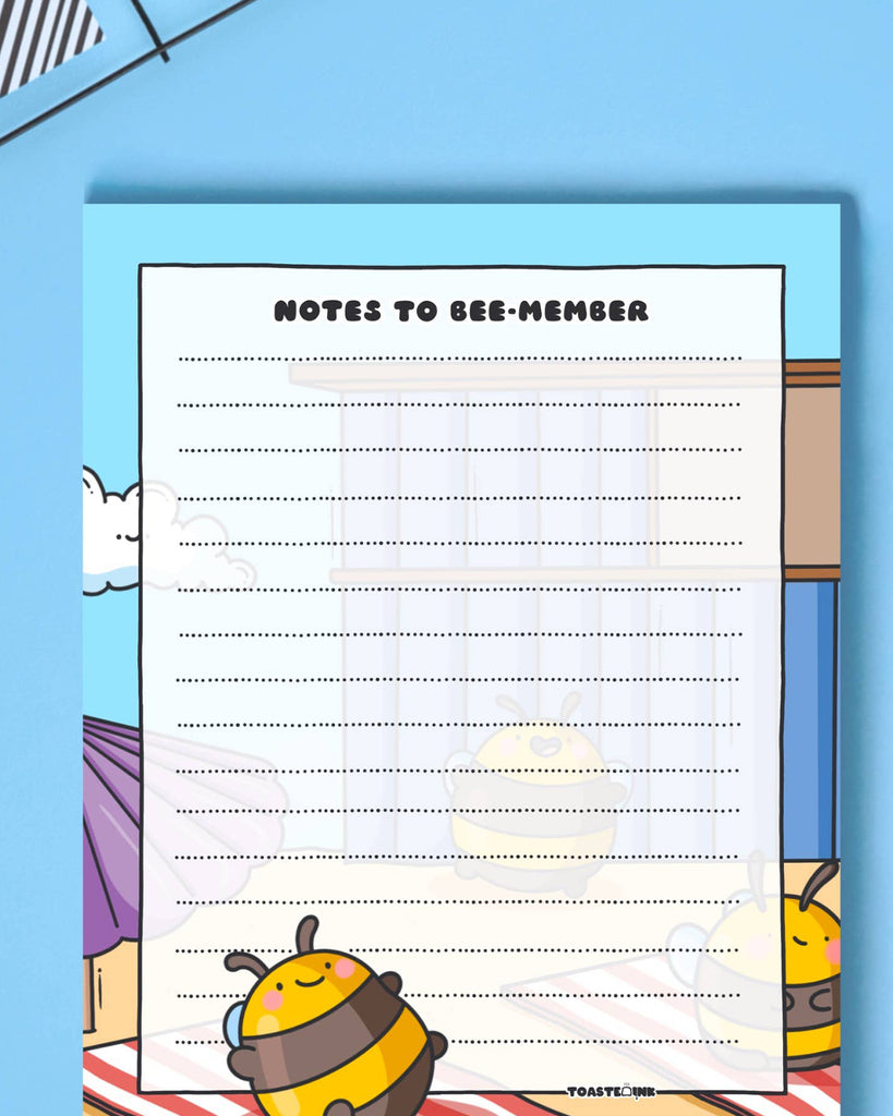 Toastedink's "Notes to Bee-member" A6 notepad sold by Rebel Romance. Features a happy bumblebee in a sunny beach scene. Displayed on a bright blue background.