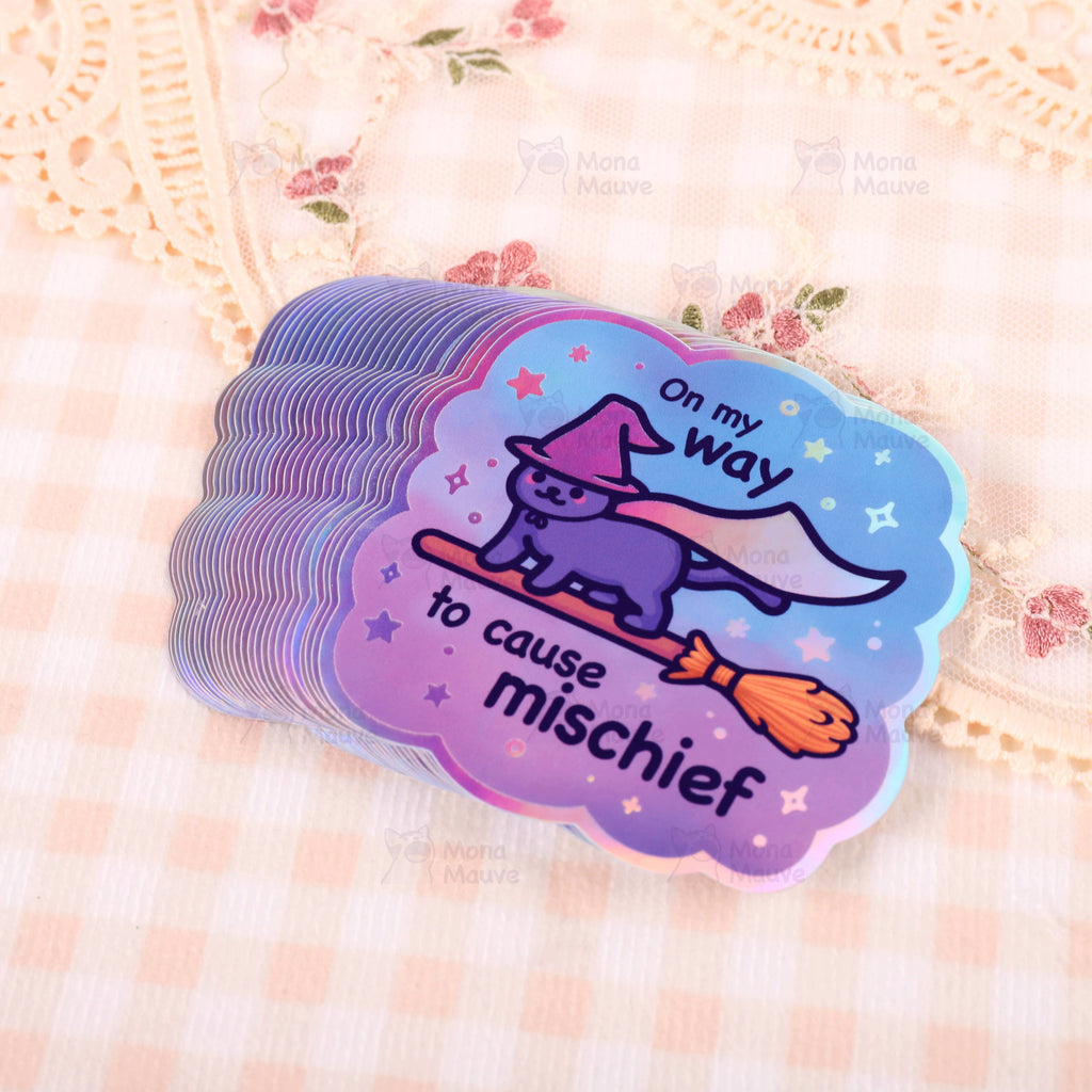 Stack of holographic "On My Way to Cause Mischief" witch cat vinyl stickers by Mona Mauve. Features a purple cat in a pointy hat flying on a broomstick, surrounded by stars. Available from Rebel Romance, a UK small business celebrating magical, whimsical, and alternative aesthetics for millennials.