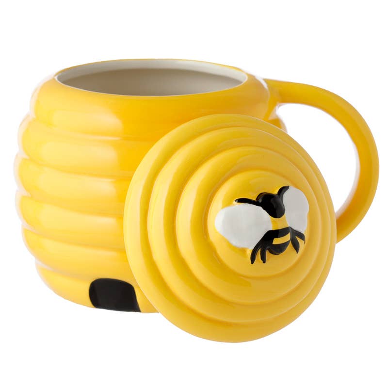 A close-up of a yellow beehive-shaped ceramic mug with a matching lid featuring a 3D bee design. Sold by Rebel Romance, a small UK brand known for quirky and alternative gifts.