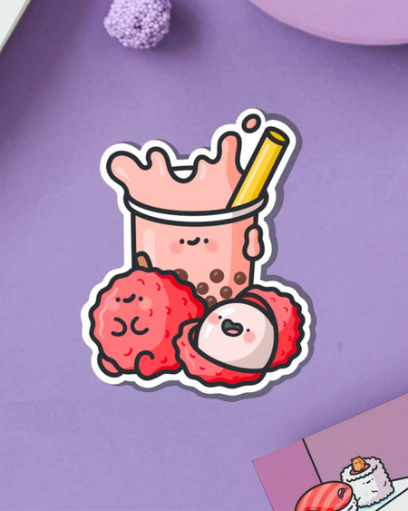 Playful sticker featuring a happy cup of lychee bubble tea and two cute lychee fruits, placed on a lilac background with a postcard nearby. A Toastedink design stocked by Rebel Romance, celebrating fun, fruity and nostalgic vibes for millennials.