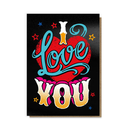 A greeting card inspired by vintage tattoo designs featuring a bold red heart, vibrant blue script reading “I Love You,” and colourful retro typography with stars against a black background. The design is enhanced with black hot foil for a textured and striking finish, paired with a recycled kraft envelope.