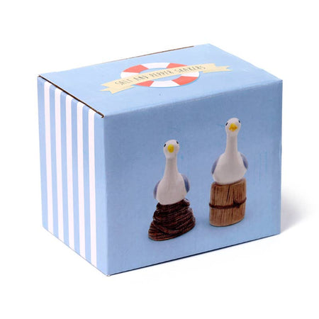 Product packaging for the Seagull Buoy Salt & Pepper Set by Rebel Romance. The box features both ceramic shakers—seagulls on a rope buoy and wooden post—against a pale blue backdrop with stripes and a life ring logo.