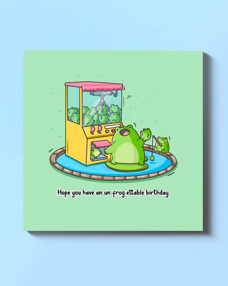 Front cover of the "Hope You Have an Un-Frog-Ettable Birthday" card by Toastedink, featuring a frog using a claw machine full of other frogs. A playful, punny design perfect for birthdays. Stocked by Rebel Romance, your go-to for alternative gifts.
