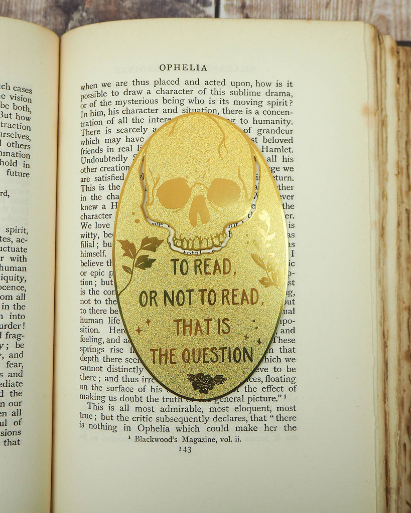 Shakespeare Hamlet Skull Brass Bookmark by Literary Emporium, engraved with “To read or not to read, that is the question”, placed on an open book. Available at Rebel Romance, a UK alternative fashion and gifts brand.