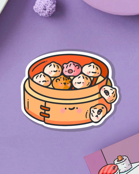Cute Steamed Buns Vinyl Sticker by Toastedink on a lilac background. Features kawaii-style steamed buns shaped like pigs, tigers and traditional dumplings in a happy bamboo steamer. Sold by Rebel Romance, a UK small biz celebrating alternative aesthetics and foodie joy.
