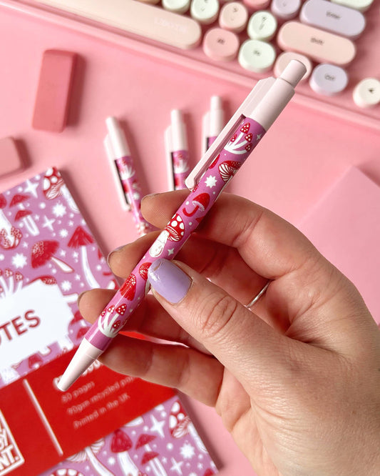 Close-up of the Pink Mushroom Pen by Rebel Romance held in hand. The pen showcases a whimsical red and white mushroom design on a pink background, perfect for stationery lovers and foragers alike.