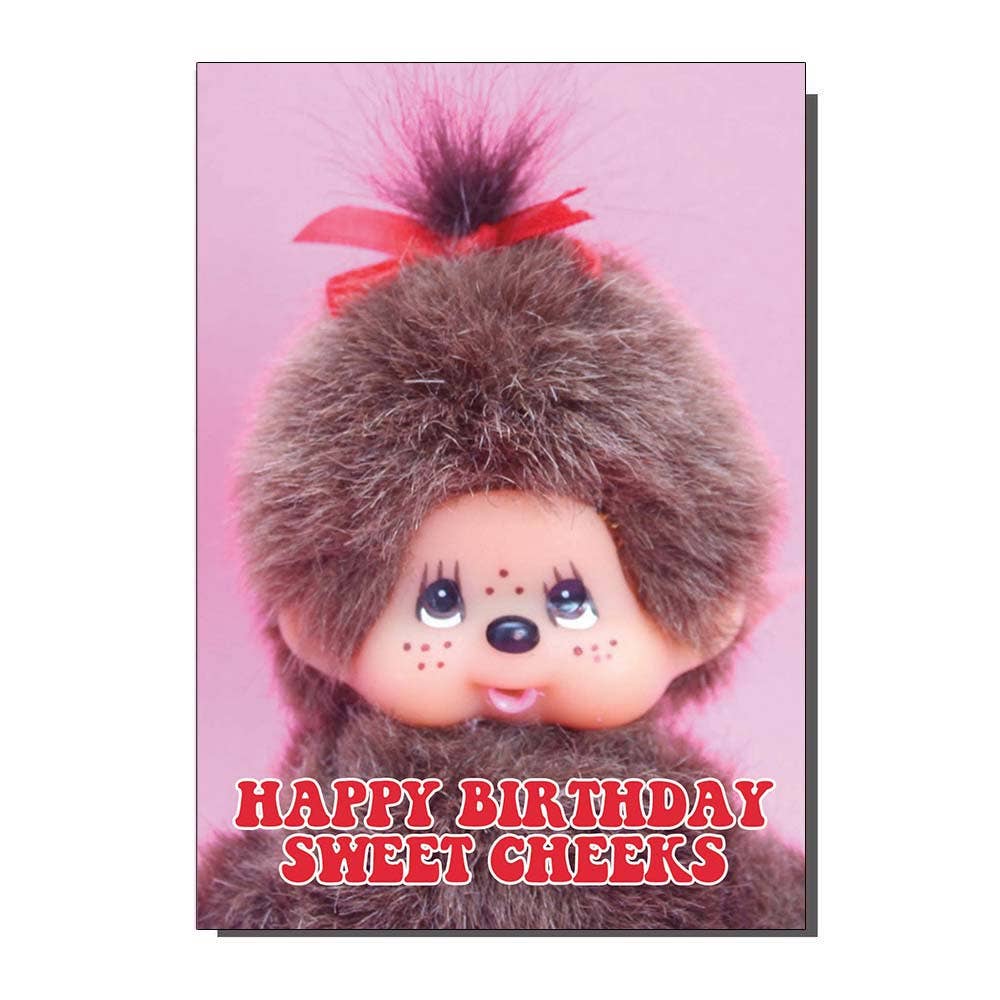 Greeting card featuring a retro-style Monchhichi doll with fluffy brown fur, pink background, and red bow, with bold red and white text that reads “Happy Birthday Sweet Cheeks.” A cheeky vintage-style birthday card design by Bite Your Granny, sold by Rebel Romance, a UK indie brand celebrating quirky, alternative fashion and gifts.
