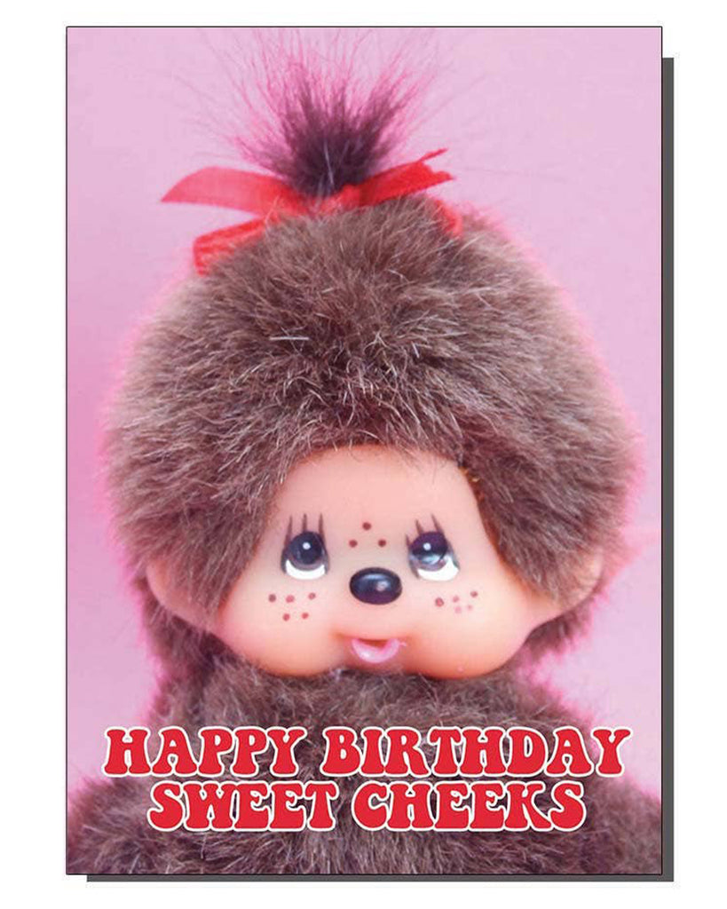 Greeting card featuring a retro-style Monchhichi doll with fluffy brown fur, pink background, and red bow, with bold red and white text that reads “Happy Birthday Sweet Cheeks.” A cheeky vintage-style birthday card design by Bite Your Granny, sold by Rebel Romance, a UK indie brand celebrating quirky, alternative fashion and gifts.