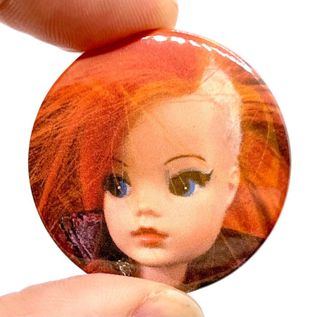 A 38mm high-gloss pin badge featuring a retro Sindy doll with bright orange punk hair and bold makeup. Designed by Bite Your Granny, celebrating offbeat nostalgia and edgy style.