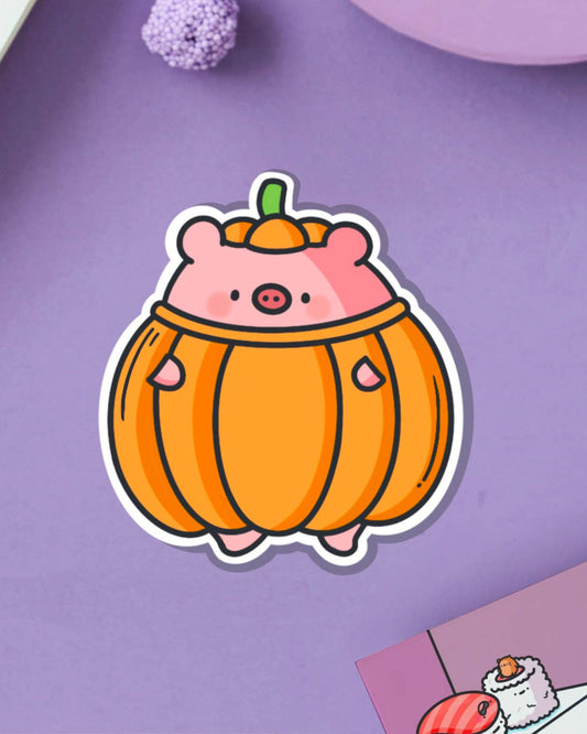 Adorable pumpkin pig vinyl sticker featuring a chubby pink pig wearing a round orange pumpkin suit with a green stem hat. Designed by Toastedink, available at Rebel Romance. Shown on a pastel purple background with cosy props. Cute waterproof sticker for seasonal or everyday fun.