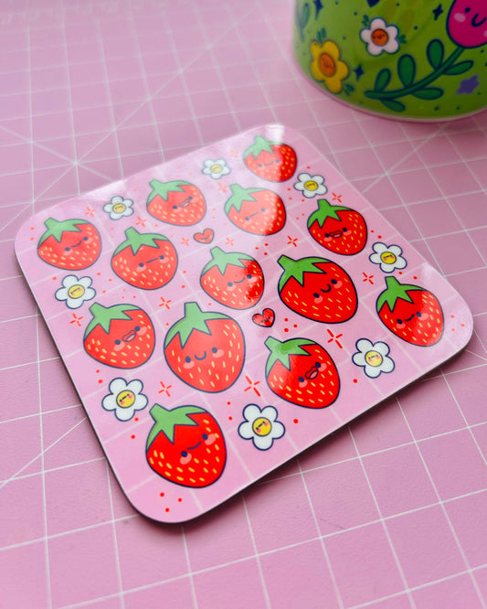 Close‑up of the Strawberry Cuties Drinks Coaster by Kelly Lou, sold by Rebel Romance. The glossy pink coaster is covered with happy red strawberries and cheerful white flowers, shown on a pastel pink cutting mat. A playful, millennial‑friendly homeware gift with a quirky vibe.