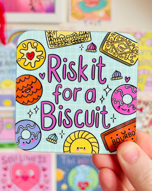 Rebel Romance “Risk It For A Biscuit” coaster by Kelly Lou held in hand, with cute illustrated biscuits like bourbons and custard creams on a blue grid design. A playful homeware gift from a UK small business that celebrates alternative aesthetics and millennial style.