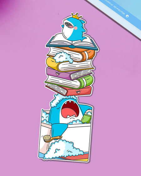 Cute shark bookmark by Toastedink for Rebel Romance, featuring a cartoon shark wearing a crown, relaxing in a bubble bath while balancing a stack of colourful books on its nose. Displayed on a purple background.