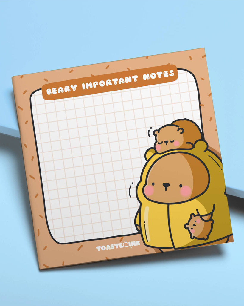 Bear-themed sticky notes from Toastedink, available at Rebel Romance, with a warm brown border, grid paper, and cute bear artwork. Displayed at an angle on a light blue backdrop.