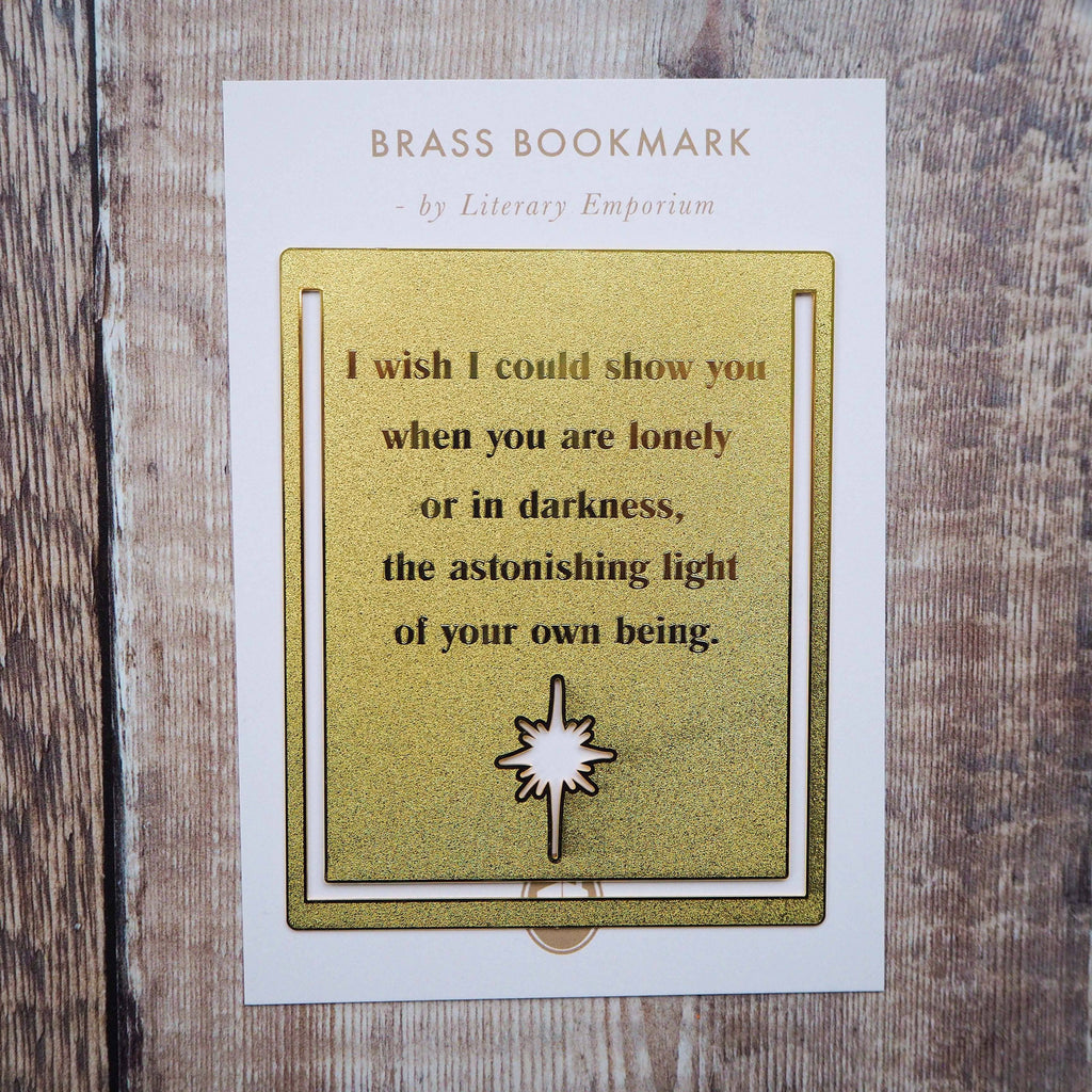A close-up image of a brass bookmark engraved with the heartfelt Hafiz of Shiraz quote: “I wish I could show you, when you are lonely or in darkness, the astonishing light of your own being.” The bookmark is resting on the pages of an open book, showcasing its intricate detailing and elegant design.