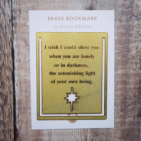 A close-up image of a brass bookmark engraved with the heartfelt Hafiz of Shiraz quote: “I wish I could show you, when you are lonely or in darkness, the astonishing light of your own being.” The bookmark is resting on the pages of an open book, showcasing its intricate detailing and elegant design.