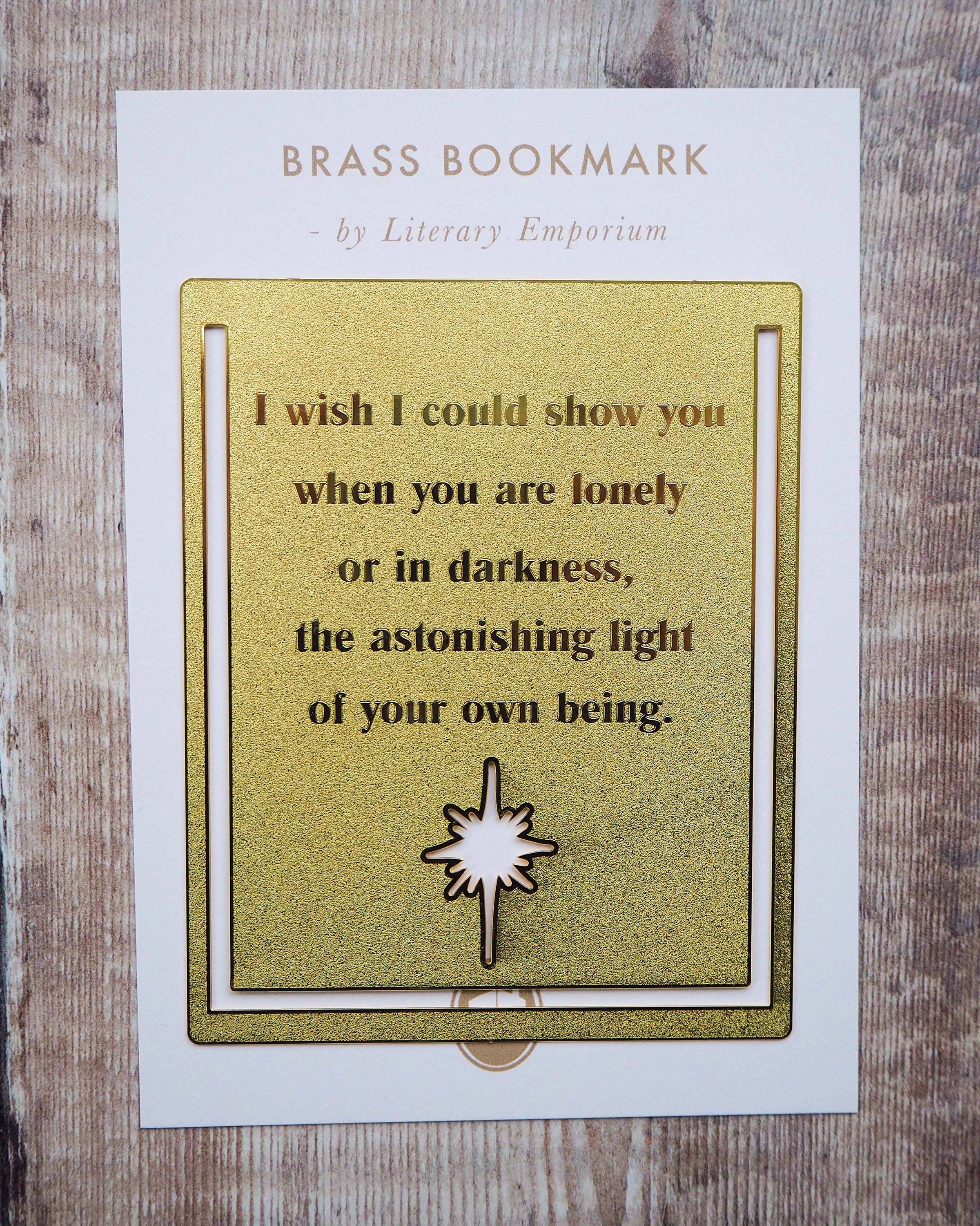 A close-up image of a brass bookmark engraved with the heartfelt Hafiz of Shiraz quote: “I wish I could show you, when you are lonely or in darkness, the astonishing light of your own being.” The bookmark is resting on the pages of an open book, showcasing its intricate detailing and elegant design.