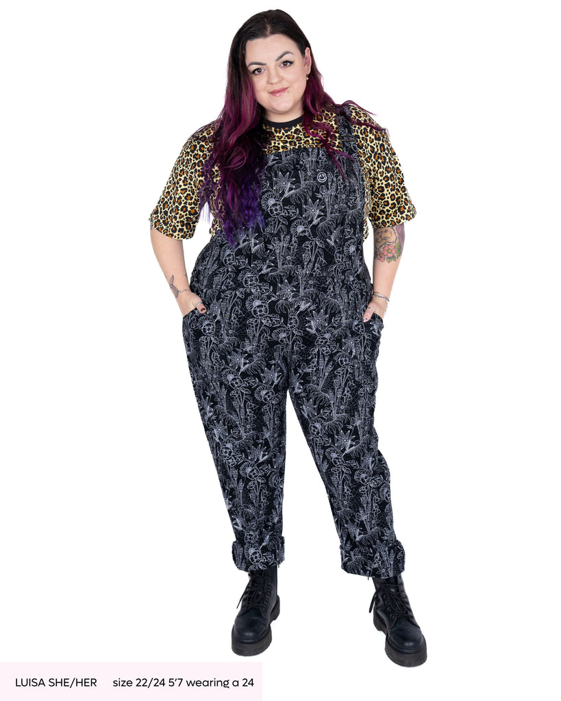 Luisa, a woman with long purple and pink curly hair wearing the rebel romance Black Floral Cobweb dungarees with the rebel romance leopard print crop top and black boots. She is facing forward smiling with her hands in the side pockets.