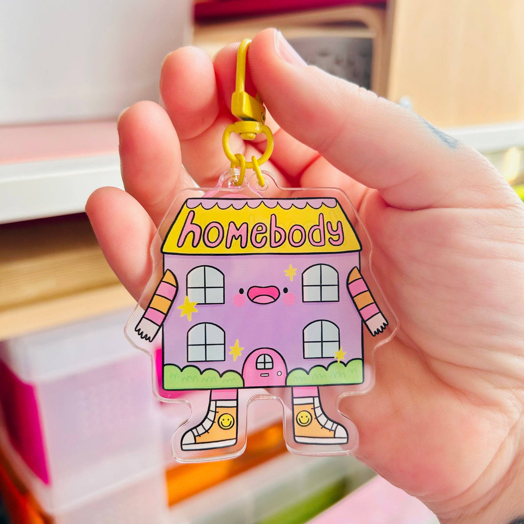 Cute lilac acrylic keyring by Kelly Lou featuring a smiling cartoon house with stripy arms and yellow shoes reading Homebody on the roof with a bright yellow clasp made from recycled acrylic and double-sided design perfect for keys or bags