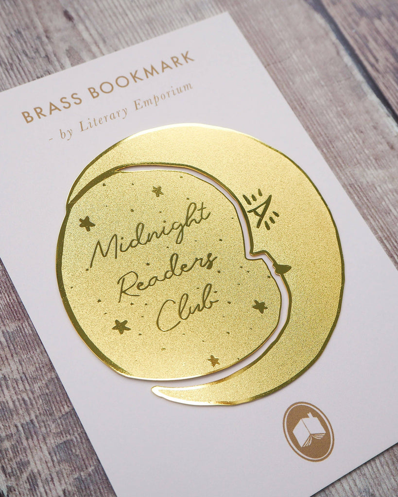 A crescent moon-shaped brass bookmark with “Midnight Readers Club” and celestial stars etched onto its surface, placed on an open book to mark a page. The bookmark adds an elegant and whimsical touch, ideal for book lovers who enjoy night-time reading.