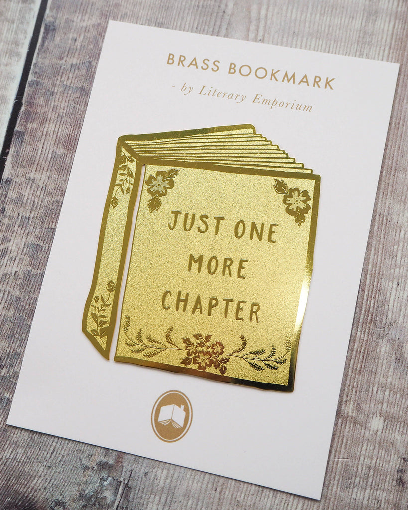A Literary Emporium brass bookmark displayed on its backing card. Shaped like a book with floral engraving and the phrase “Just One More Chapter.” Stocked by Rebel Romance, a UK small business for alternative gifts and ethical fashion.