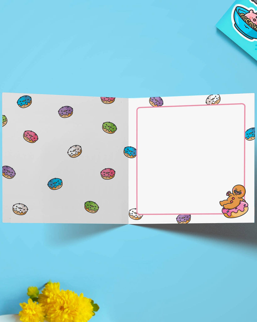 Inside view of a Toastedink donut-themed birthday card, showing patterned illustrations of colourful frosted donuts and a framed space to write a message, with a mini gingerbread character sitting on a donut.