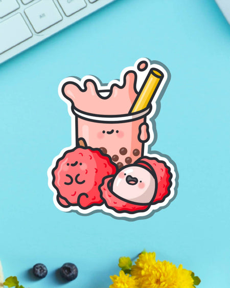 Adorable lychee bubble tea vinyl sticker featuring a kawaii cup of boba and two lychee fruits, placed on a bright blue background near a keyboard. Stocked by Rebel Romance, a UK indie brand embracing quirky, nostalgic and alternative aesthetics.