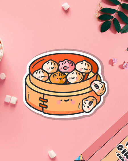 Kawaii-style Steamed Buns Vinyl Sticker by Toastedink on a pink flat lay. Features smiling animal and traditional bun characters in a bamboo steamer. Sold by Rebel Romance, a UK-based alternative lifestyle brand for millennials who love quirky, food-inspired art.