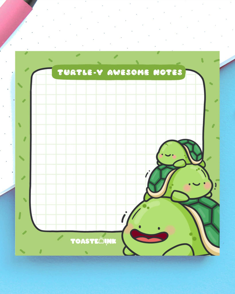 Close-up of square sticky notes with happy cartoon turtles stacked in the corner. The green pad features grid lines and the punny header “Turtle-y Awesome Notes.” Sold by Rebel Romance, a UK brand known for quirky, alternative stationery and gifts.