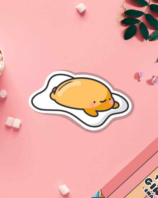 Kawaii fried egg vinyl sticker by Toastedink featuring a cute blushing egg character lounging on its whites. Displayed on a pastel pink background, this adorable sticker is sold by Rebel Romance, a UK-based alternative gift shop for quirky millennials.