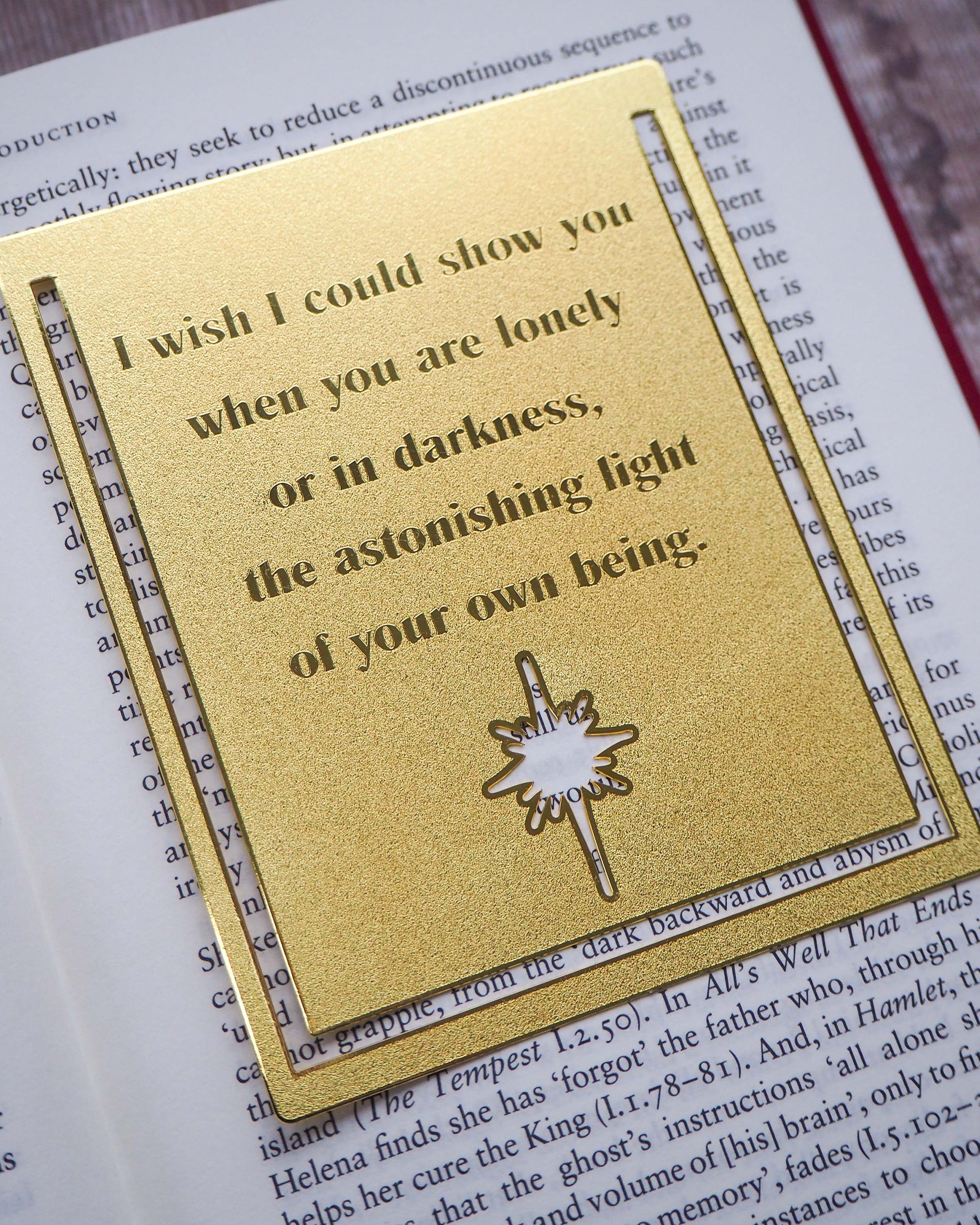 A close-up image of a brass bookmark engraved with the heartfelt Hafiz of Shiraz quote: “I wish I could show you, when you are lonely or in darkness, the astonishing light of your own being.” The bookmark is resting on the pages of an open book, showcasing its intricate detailing and elegant design.