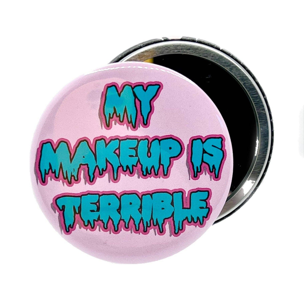 Round pink pocket mirror with bold dripping text that reads “My Makeup Is Terrible” in turquoise and magenta, inspired by Drag Race. Designed by Bite Your Granny and sold by Rebel Romance, a small UK business celebrating alternative style and humour through bold gifts and accessories for millennials.