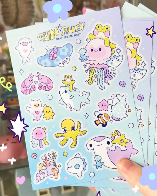 A close-up of multiple A6 Ocean Sticker Sheets by Sun Puff Studios, stocked by Rebel Romance. Each sheet features cute sea creatures like jellyfish, narwhals, frogs, stingrays, clownfish, and octopuses in pastel tones. Perfect for adding charm to journals, planners or letters.