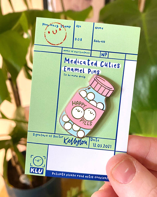 A cute enamel pin from Rebel Romance shaped like a pink bottle labelled “Happy Pills”, filled with smiling tablets. Designed by Kellylou, this mental health and spoonie pride pin is displayed on a green pharmacy‑style backing card with playful handwriting details. A perfect gift for alternative fashion lovers and millennial collectors.
