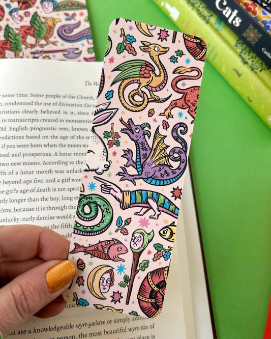 An aesthetic pastel bookmark covered in whimsical medieval creatures including dragons, moons, snails, and strange plants. Designed by Stacey McEvoy Caunt, this double-sided bookmark is sold by Rebel Romance, an alternative UK indie brand.