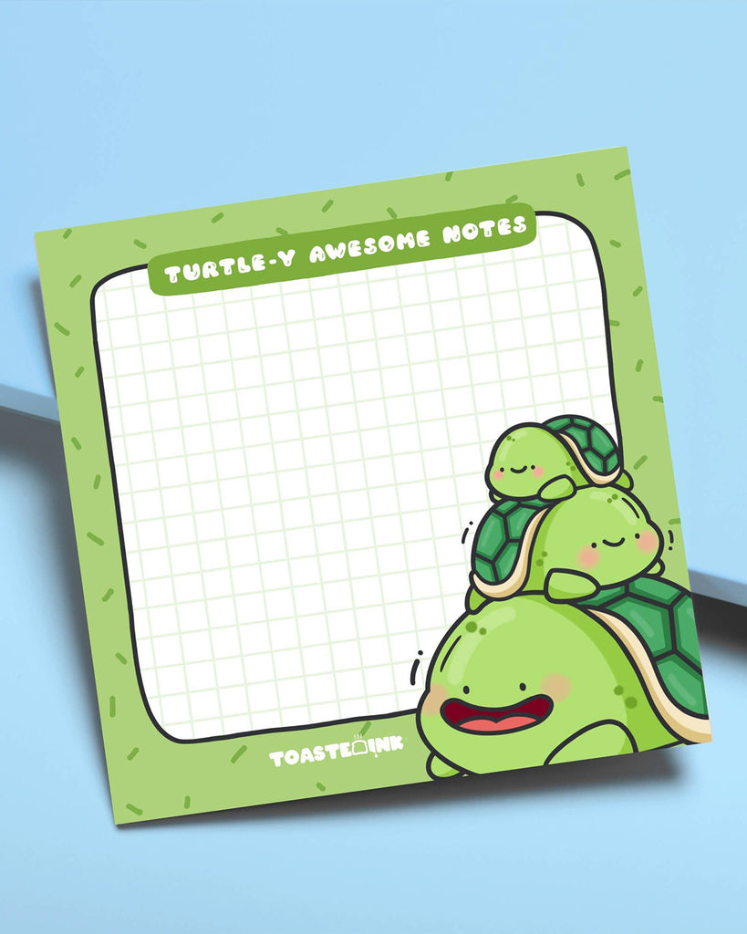 Angled photo of Toastedink’s Turtle-y Awesome Sticky Notes with a stack of three adorable turtles. Green grid layout with fun sprinkles border, perfect for jotting cute reminders. Sold by Rebel Romance, a UK small business celebrating whimsical and arty aesthetics.