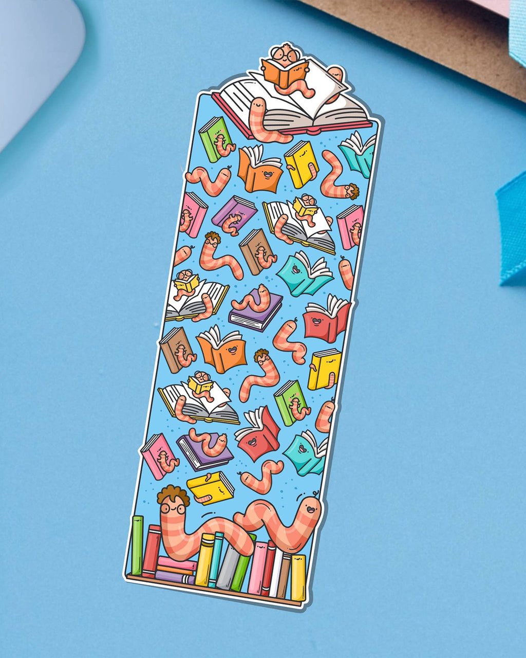 Cute and colourful bookworm bookmark designed by Toastedink, available at Rebel Romance, with a worm reading atop a book stack and more worms among floating books. Set against a bright blue background.